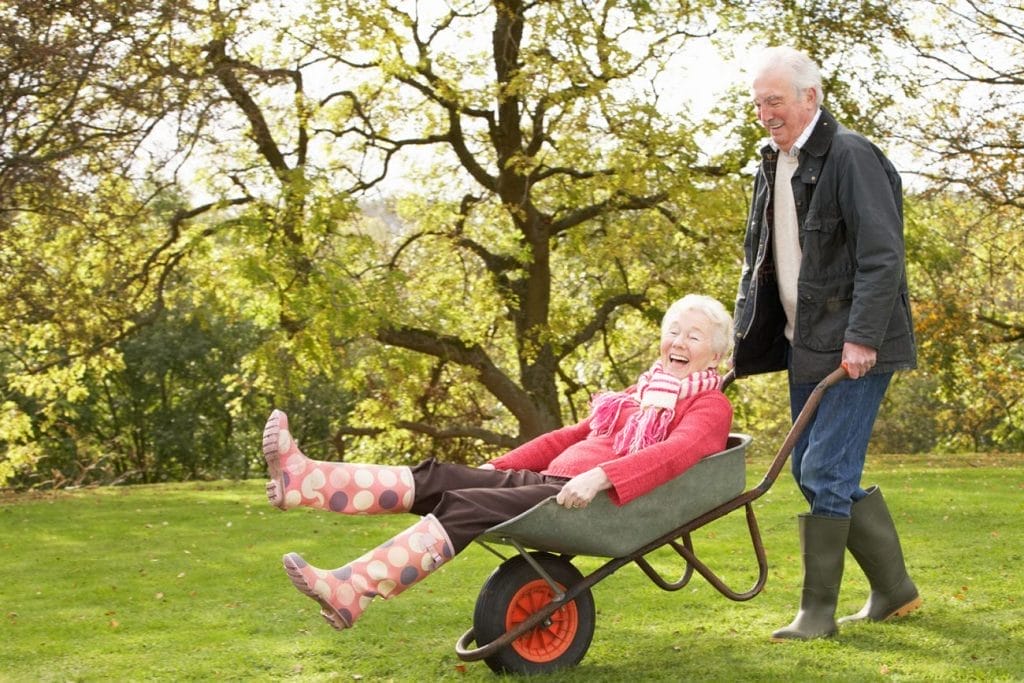An elderly couple using home care services pushing a wheelbarrow in a park.