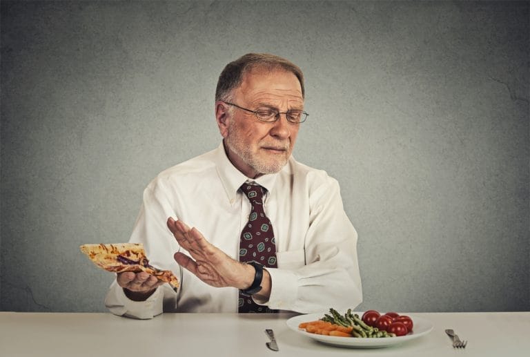 A man eating a slice of pizza and vegetables to help manage high blood pressure in seniors.