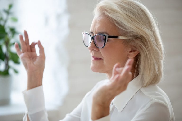 A woman wearing glasses is making a gesture with her hands to alleviate high blood pressure in seniors.