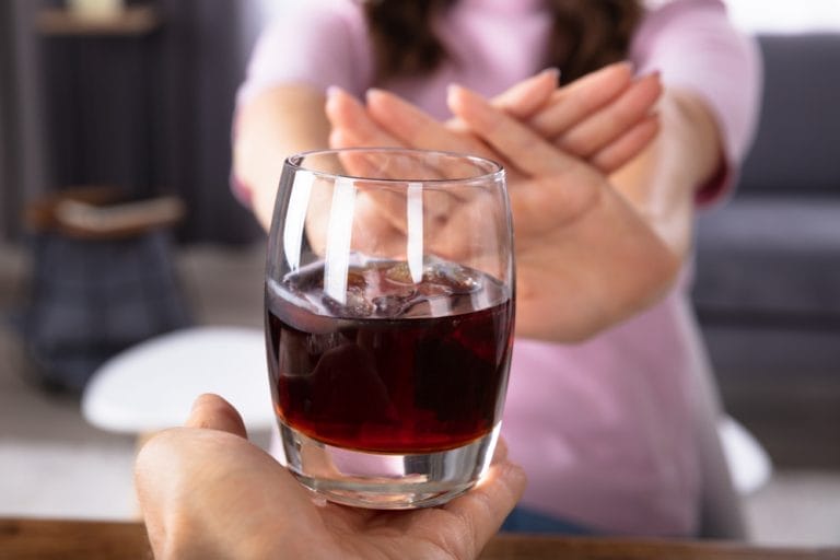 A woman carefully offering a glass of red wine to another person, potentially exacerbating high blood pressure in seniors.