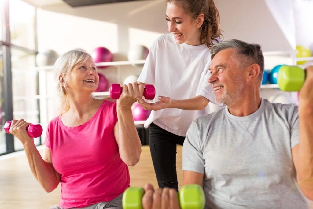 A woman and an older man exercising with dumbbells at a home gym
