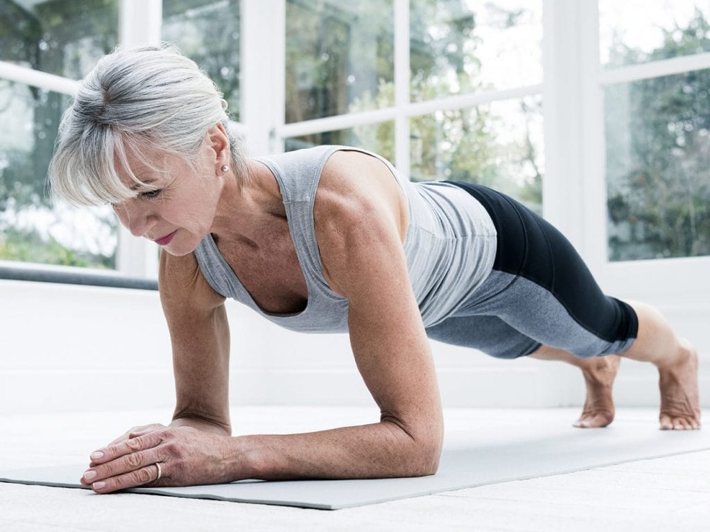 An elderly woman performing safe planks on a mat.