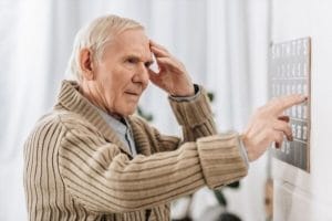 An elderly man with dementia pointing at a wall calendar.