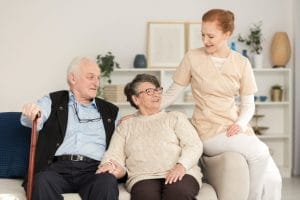 Two elderly people sitting on a couch with a nurse.