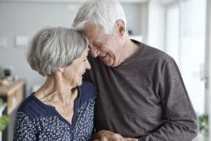 An older couple embracing each other in the kitchen.