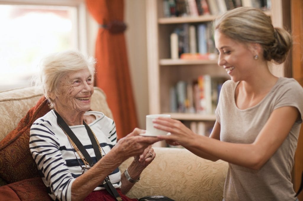 A woman giving a cup of coffee to an elderly woman.