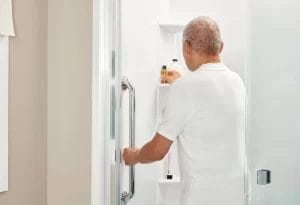 A man ensuring bathroom safety for seniors by opening the door of a shower.