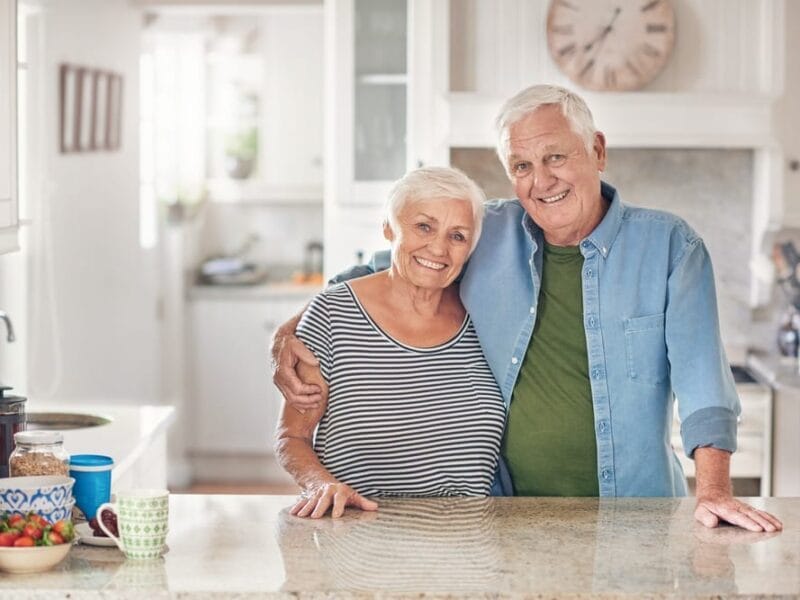 An aging couple posing for a photo in their kitchen after a hospital visit.