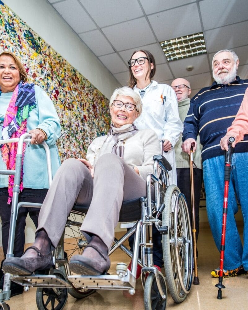 A group of elderly people in wheelchairs walking down a hallway. A group of elderly people in wheelchairs walking down a hallway.